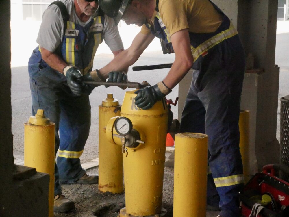 Two field workers performing maintenance on a hydrant at an active job site