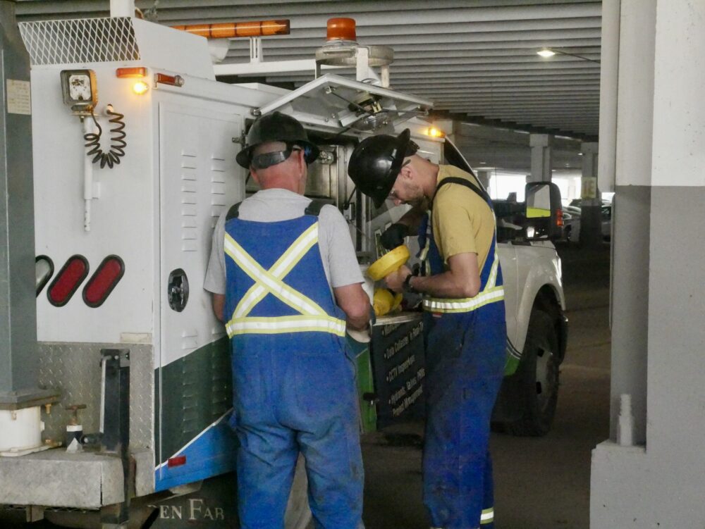 Two field workers servicing hydrant components beside a Cam-Trac service truck
